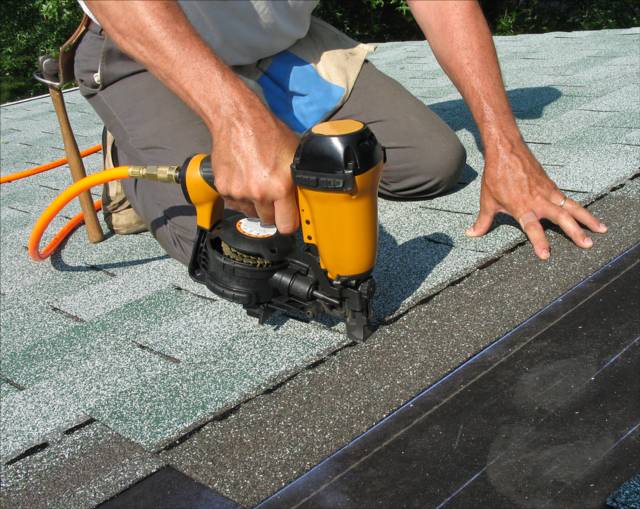 A StormForce Roofing crew member installing new shingles on a roof with a nail gun.