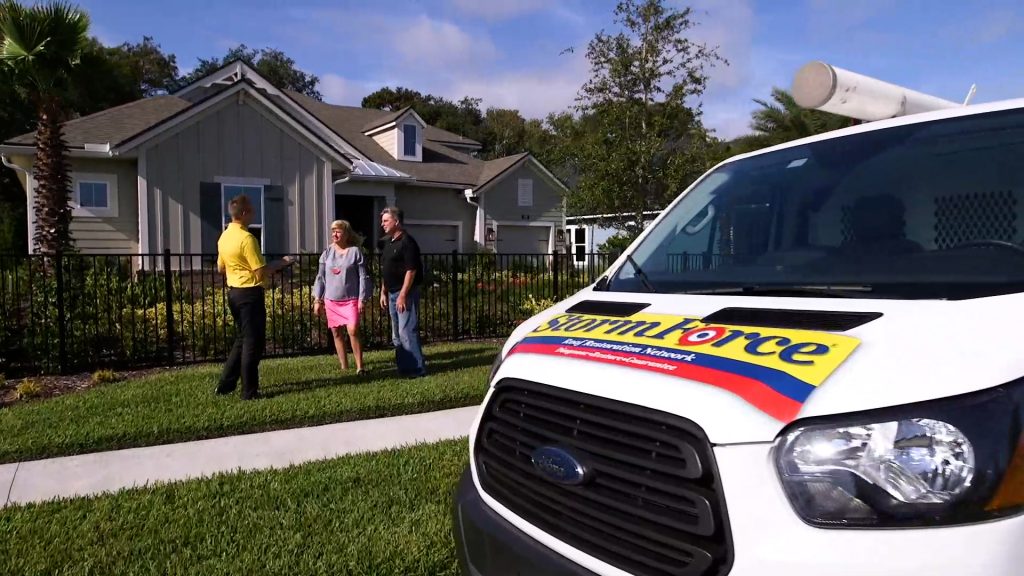 A StormForce employee speaking with two homeowners in the front yard of their home.