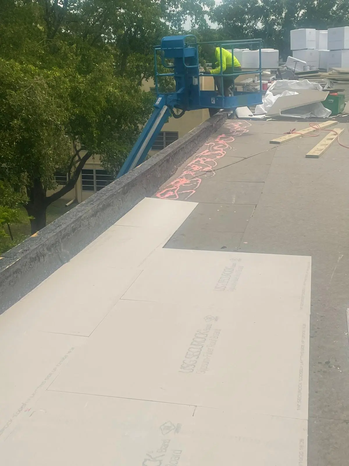 An in-progress roofing project showing insulation boards laid out on a flat roof with a boom lift in the background.